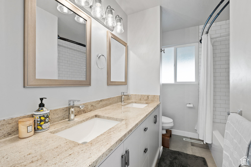 Full bathroom featuring dual vanity, tile floors, shower / bath combo with shower curtain, and toilet
