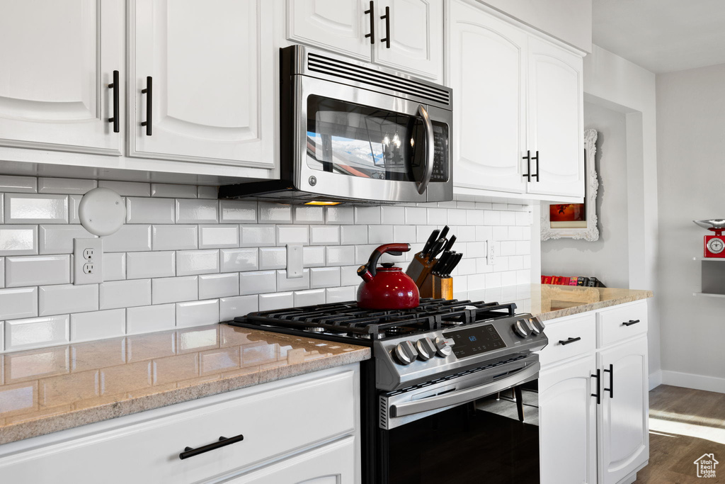 Kitchen featuring white cabinets, dark hardwood / wood-style floors, tasteful backsplash, and stainless steel appliances