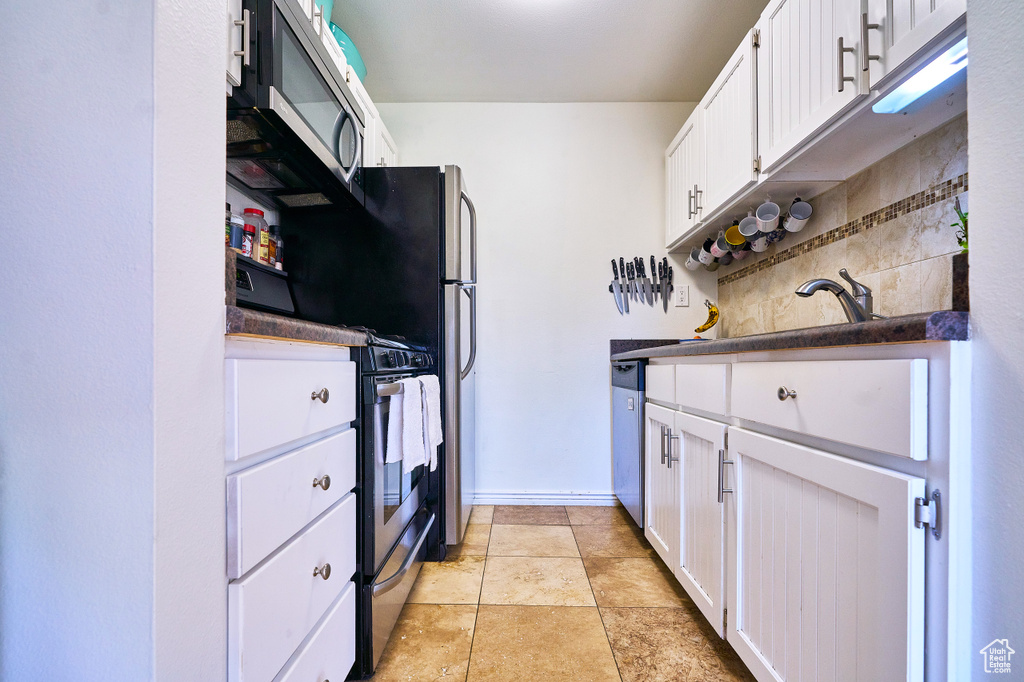 Kitchen featuring white cabinets, tasteful backsplash, light tile flooring, and stainless steel appliances