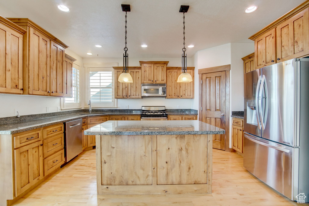 Kitchen with appliances with stainless steel finishes, pendant lighting, light hardwood / wood-style flooring, and a center island