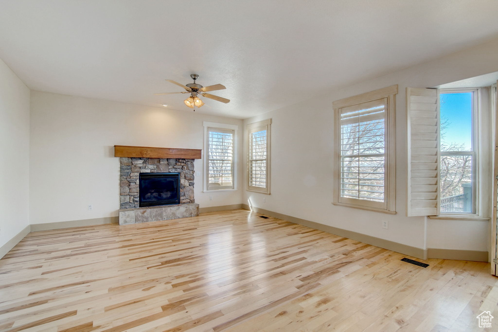 Unfurnished living room with a stone fireplace, ceiling fan, and light wood-type flooring