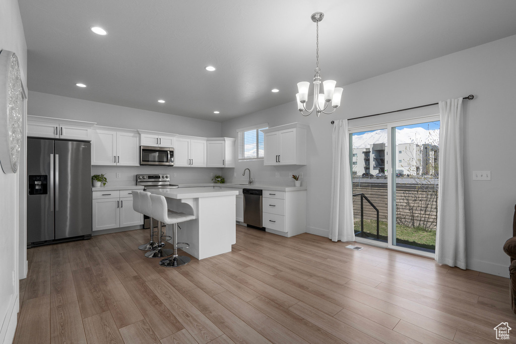 Kitchen with white cabinetry, stainless steel appliances, pendant lighting, and light wood-type flooring
