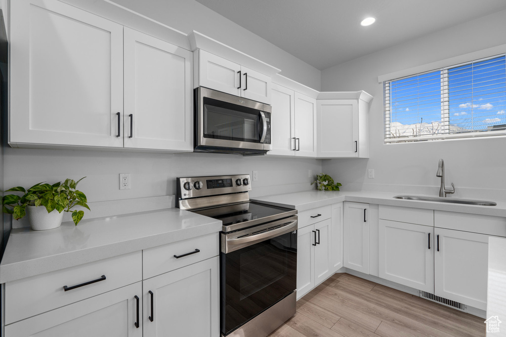 Kitchen featuring light hardwood / wood-style floors, stainless steel appliances, white cabinetry, and sink