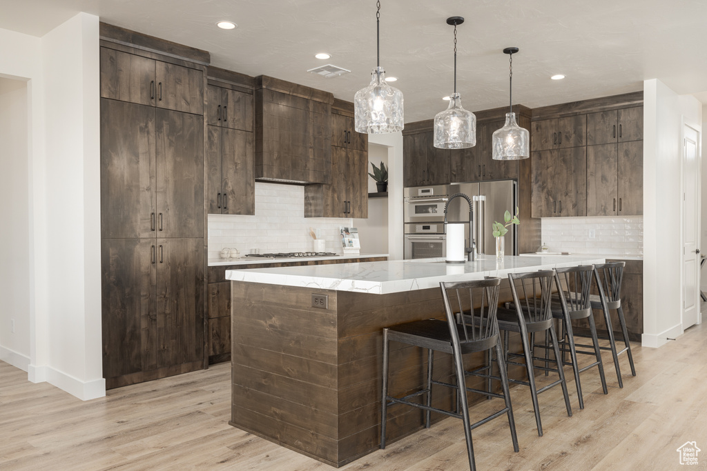 Kitchen with dark brown cabinetry, appliances with stainless steel finishes, light wood-type flooring, and backsplash