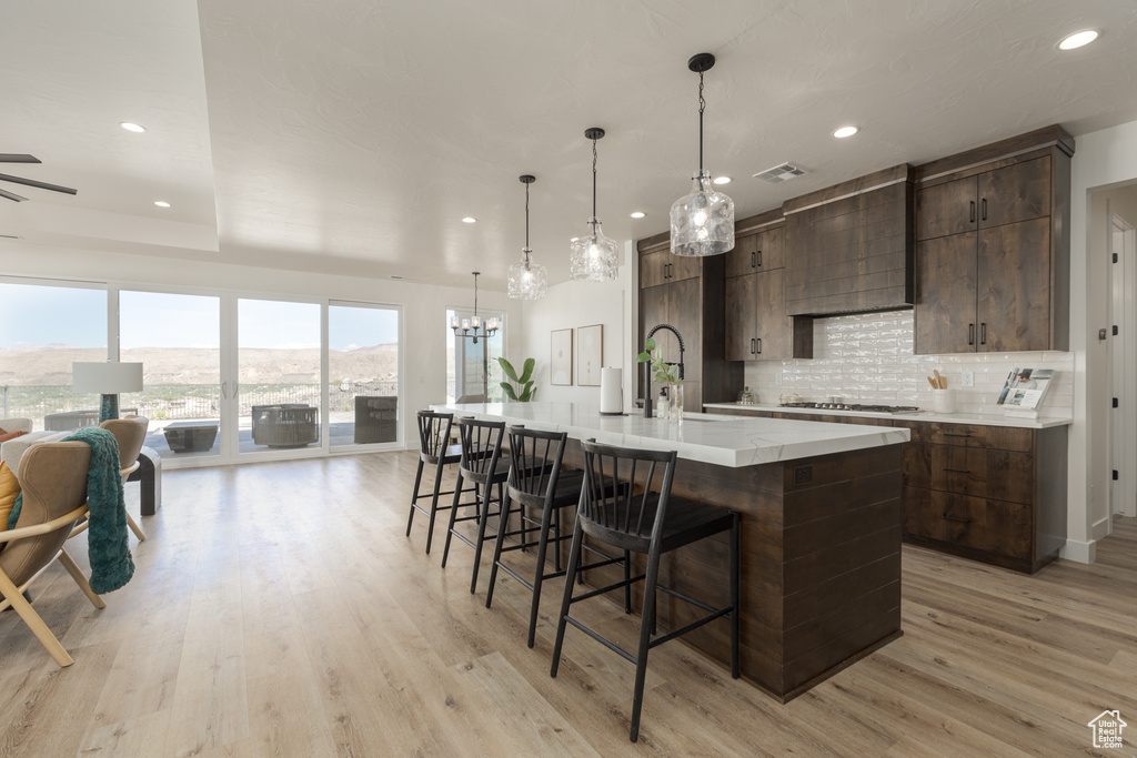 Kitchen featuring dark brown cabinets, decorative backsplash, light hardwood / wood-style floors, a large island with sink, and a kitchen breakfast bar