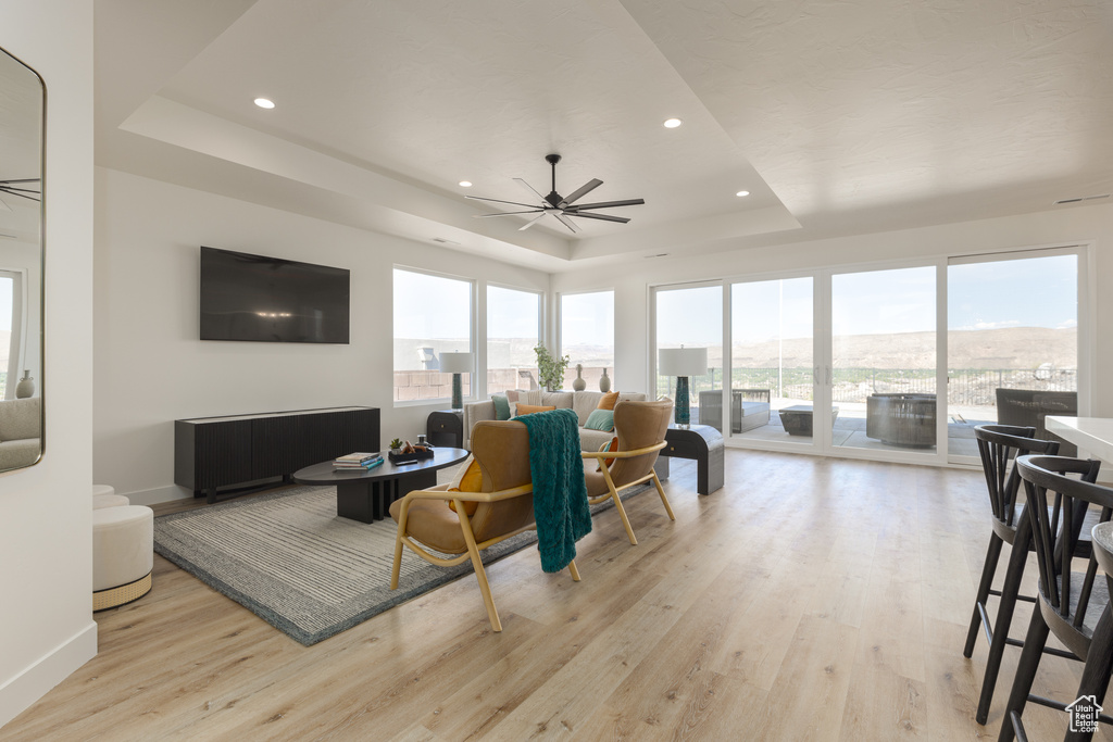 Living room with ceiling fan, light wood-type flooring, and a tray ceiling