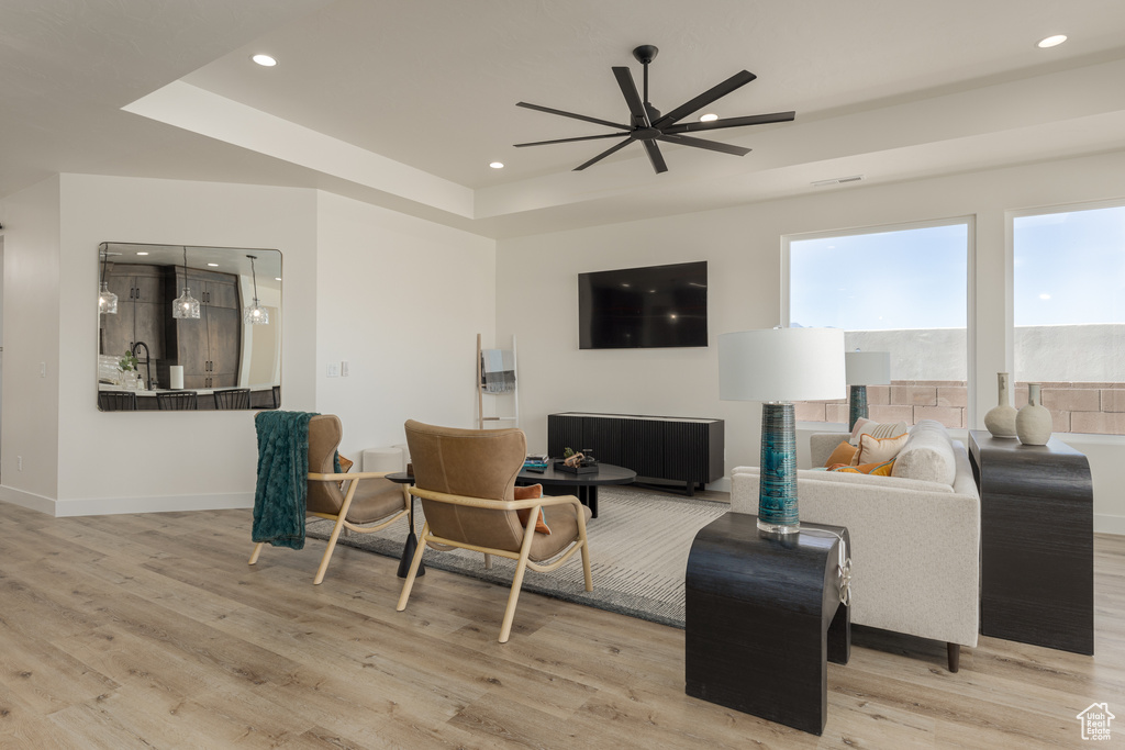 Living room featuring sink, light wood-type flooring, ceiling fan, and a raised ceiling