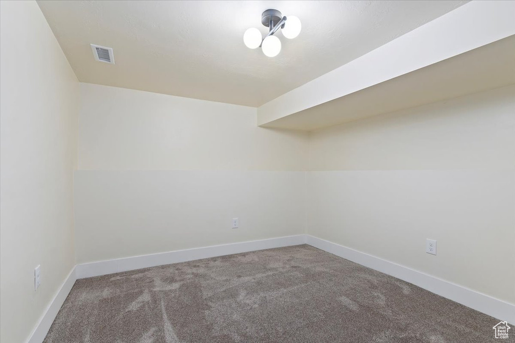 Empty room featuring light colored carpet and a notable chandelier