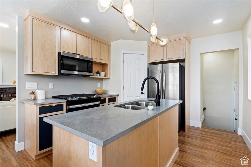 Kitchen featuring appliances with stainless steel finishes, hanging light fixtures, light wood-type flooring, sink, and a kitchen island with sink