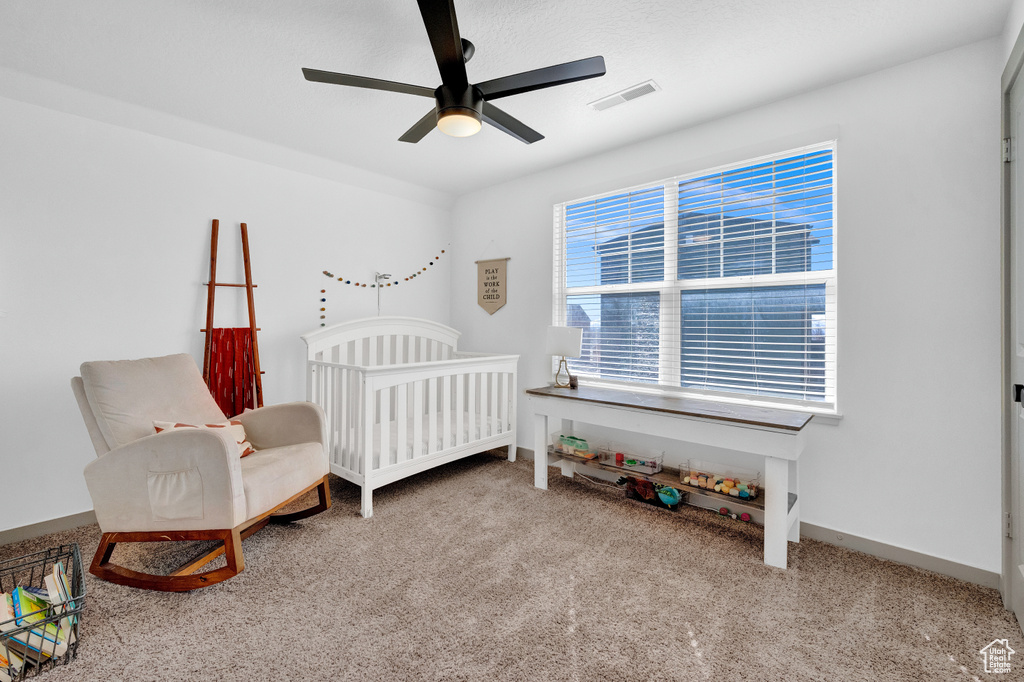 Carpeted bedroom featuring ceiling fan and a crib