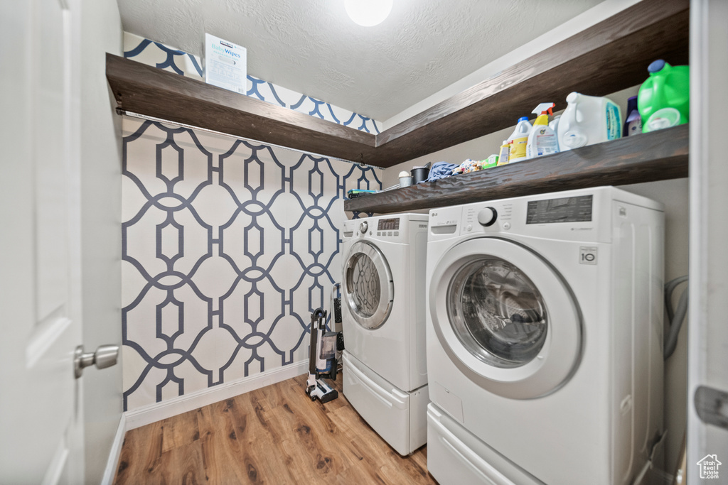Laundry room with light hardwood / wood-style flooring, washer and clothes dryer, and a textured ceiling