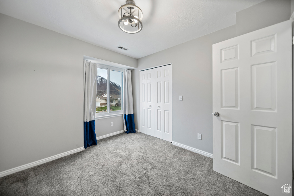 Unfurnished bedroom featuring a chandelier, light colored carpet, and a closet