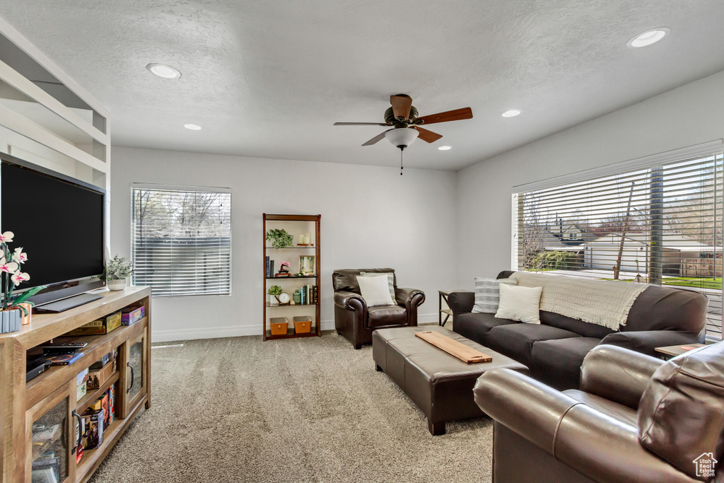Living room with a textured ceiling, ceiling fan, a wealth of natural light, and light colored carpet