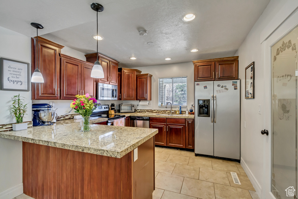 Kitchen featuring kitchen peninsula, sink, stainless steel appliances, light tile flooring, and decorative light fixtures