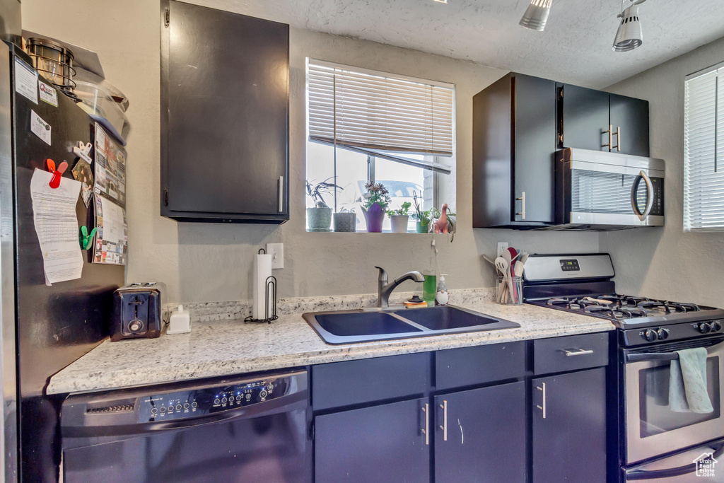 Kitchen with appliances with stainless steel finishes, sink, plenty of natural light, and light stone countertops