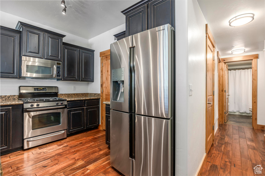 Kitchen featuring appliances with stainless steel finishes, light stone countertops, and dark wood-type flooring