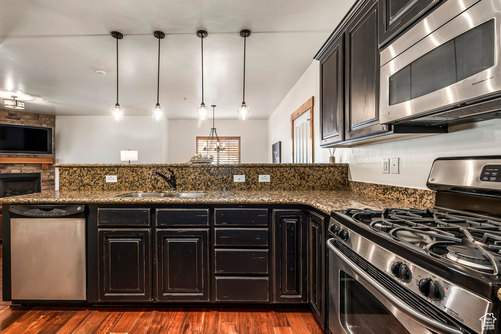 Kitchen featuring appliances with stainless steel finishes, pendant lighting, dark wood-type flooring, dark stone countertops, and sink