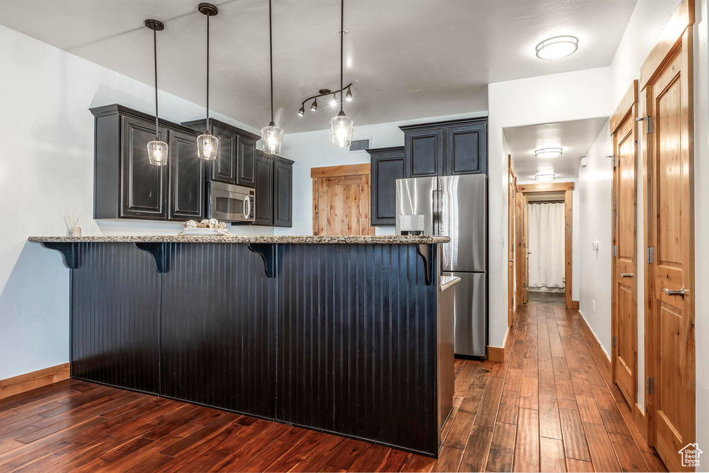 Kitchen featuring decorative light fixtures, dark wood-type flooring, light stone counters, rail lighting, and stainless steel appliances