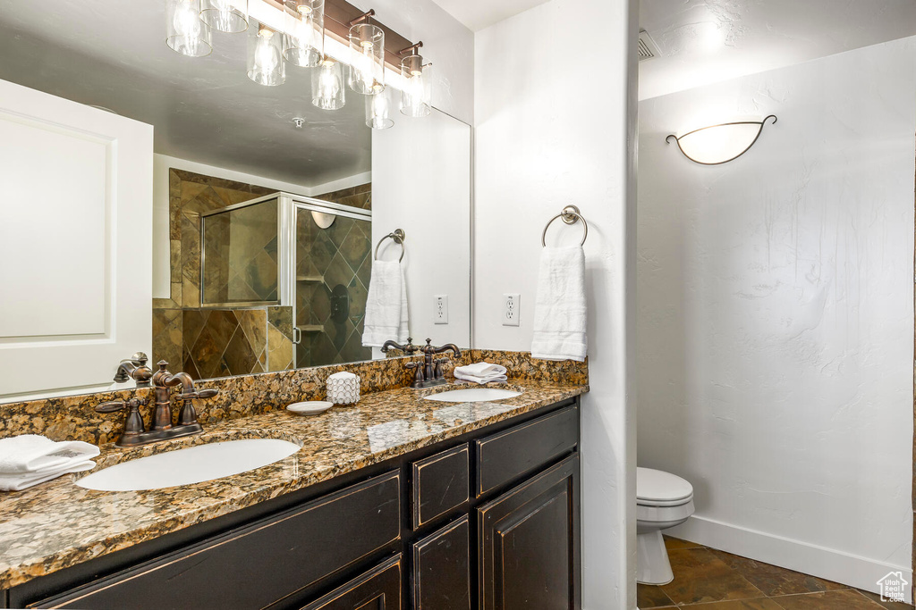 Bathroom with toilet, a shower with shower door, vanity with extensive cabinet space, dual sinks, and tile floors