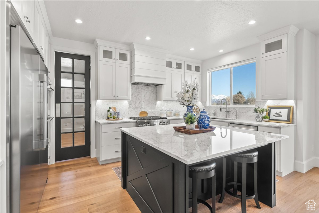 Kitchen with white cabinets, light hardwood / wood-style flooring, premium range hood, and a center island