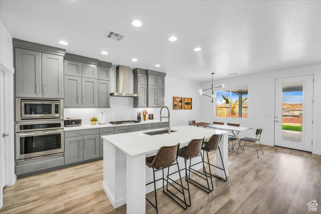 Kitchen featuring a notable chandelier, appliances with stainless steel finishes, sink, light hardwood / wood-style flooring, and wall chimney exhaust hood