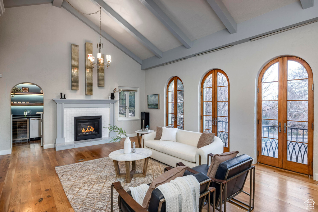 Living room featuring beamed ceiling, a brick fireplace, wine cooler, light wood-type flooring, and french doors