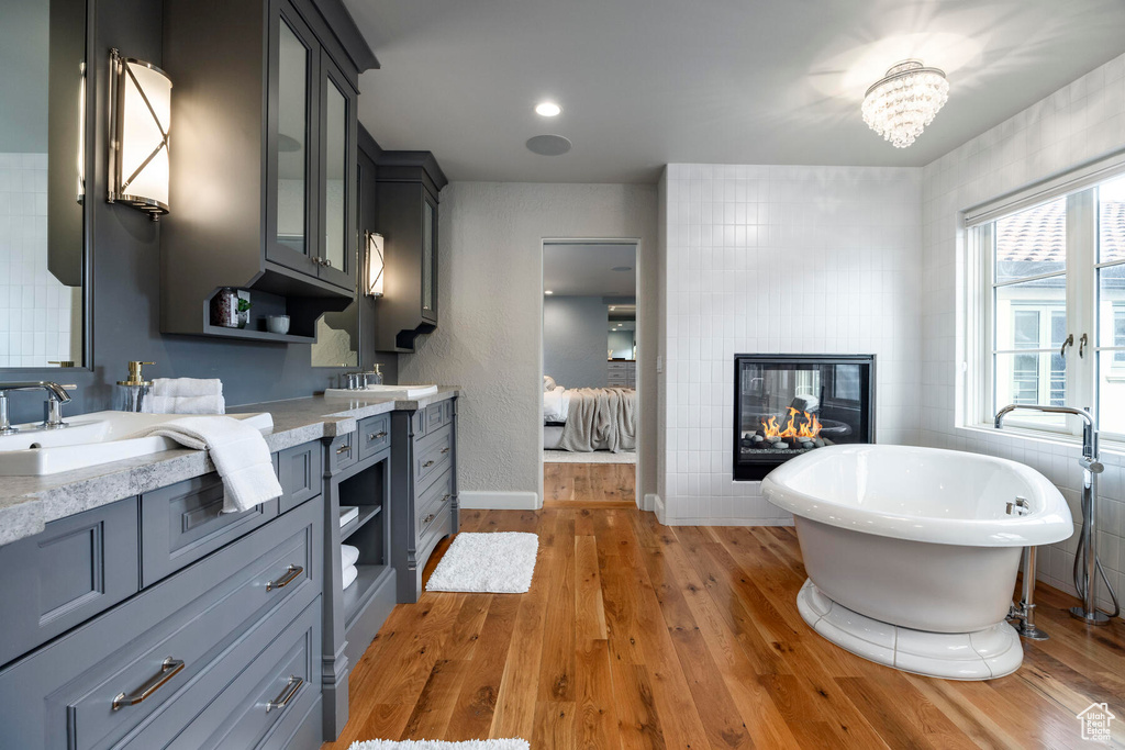 Bathroom with tile walls, a multi sided fireplace, vanity, hardwood / wood-style flooring, and a tub