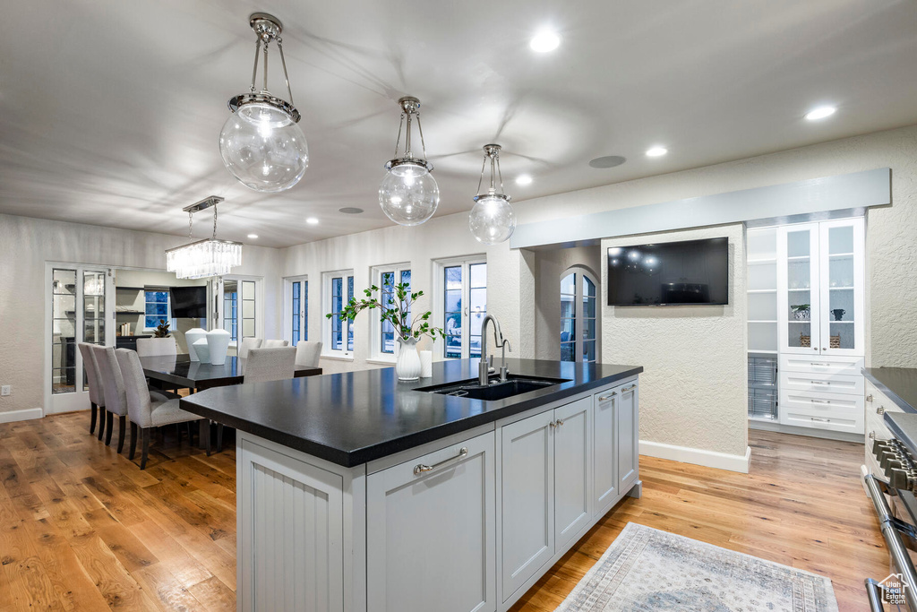 Kitchen with an island with sink, white cabinets, sink, pendant lighting, and light wood-type flooring