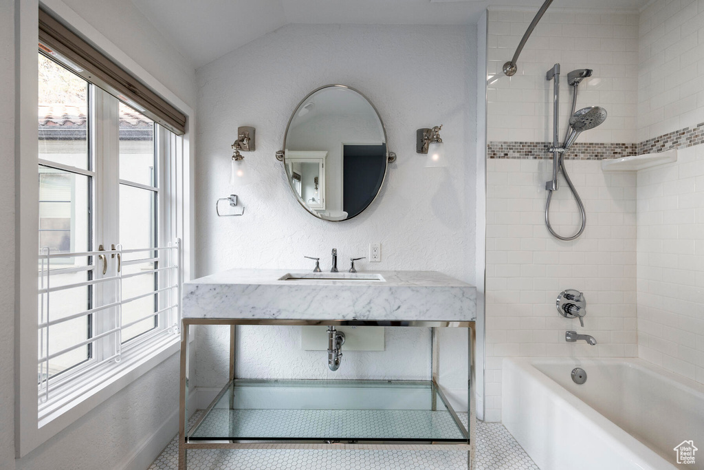 Bathroom featuring vaulted ceiling, tiled shower / bath, vanity, and tile floors