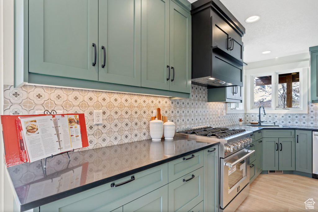 Kitchen with sink, light hardwood / wood-style floors, backsplash, high end stainless steel range, and green cabinets