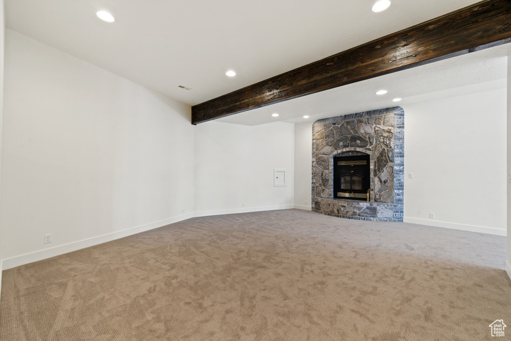 Unfurnished living room with light carpet, beam ceiling, and a fireplace