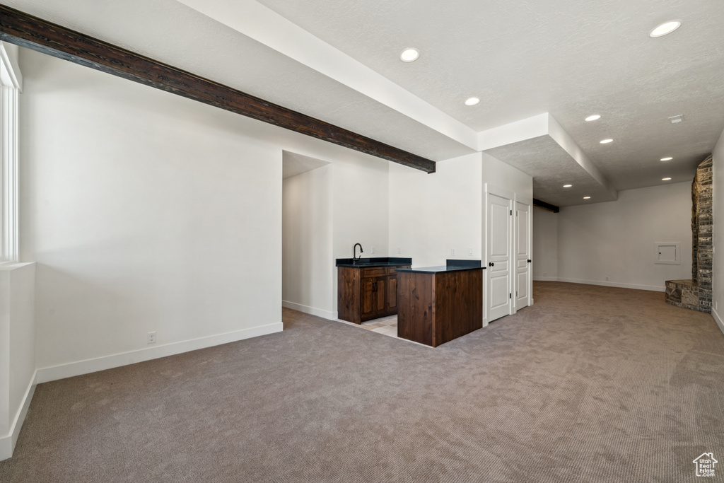 Unfurnished living room featuring beamed ceiling, brick wall, and light colored carpet