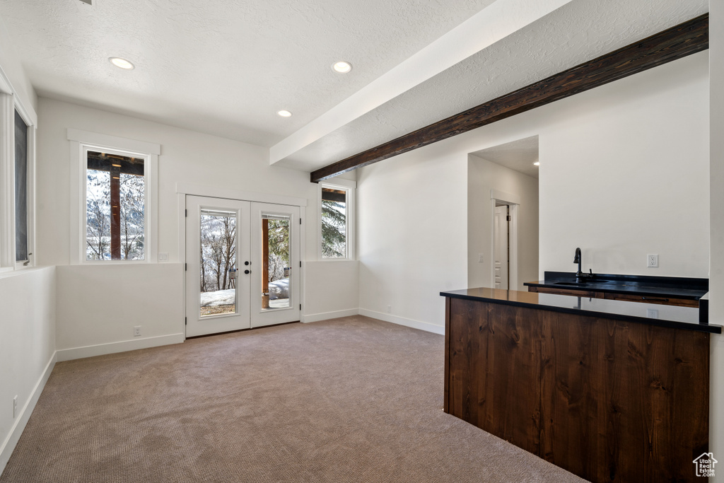 Interior space featuring light carpet, french doors, beam ceiling, sink, and a textured ceiling