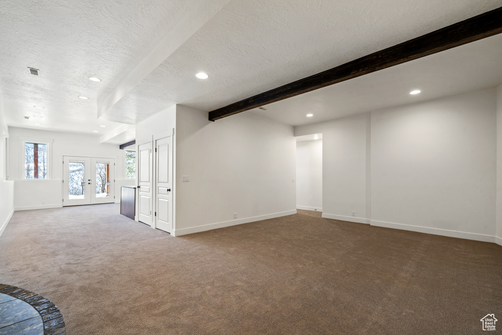 Carpeted spare room with beamed ceiling, a textured ceiling, and french doors