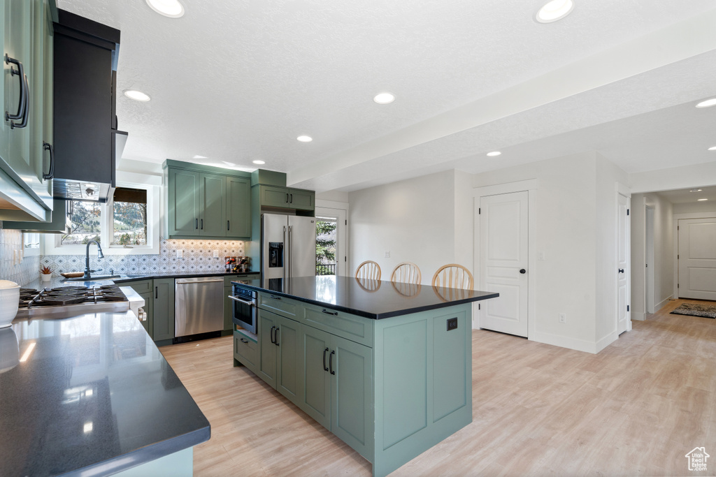 Kitchen with a kitchen island, light hardwood / wood-style flooring, appliances with stainless steel finishes, green cabinets, and tasteful backsplash