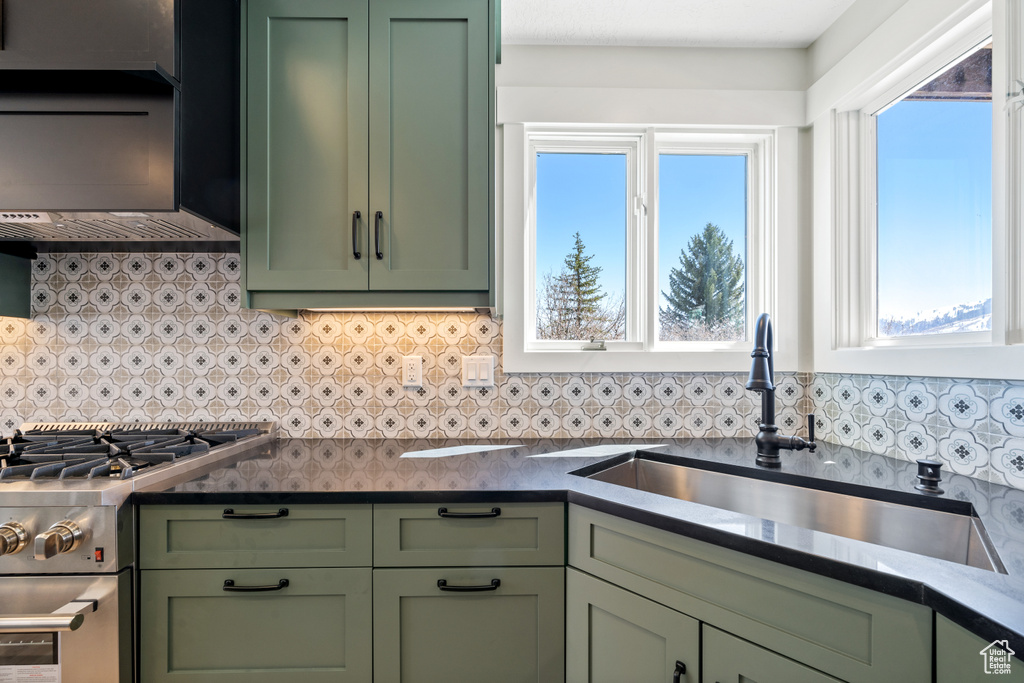 Kitchen with green cabinetry, tasteful backsplash, sink, and gas range