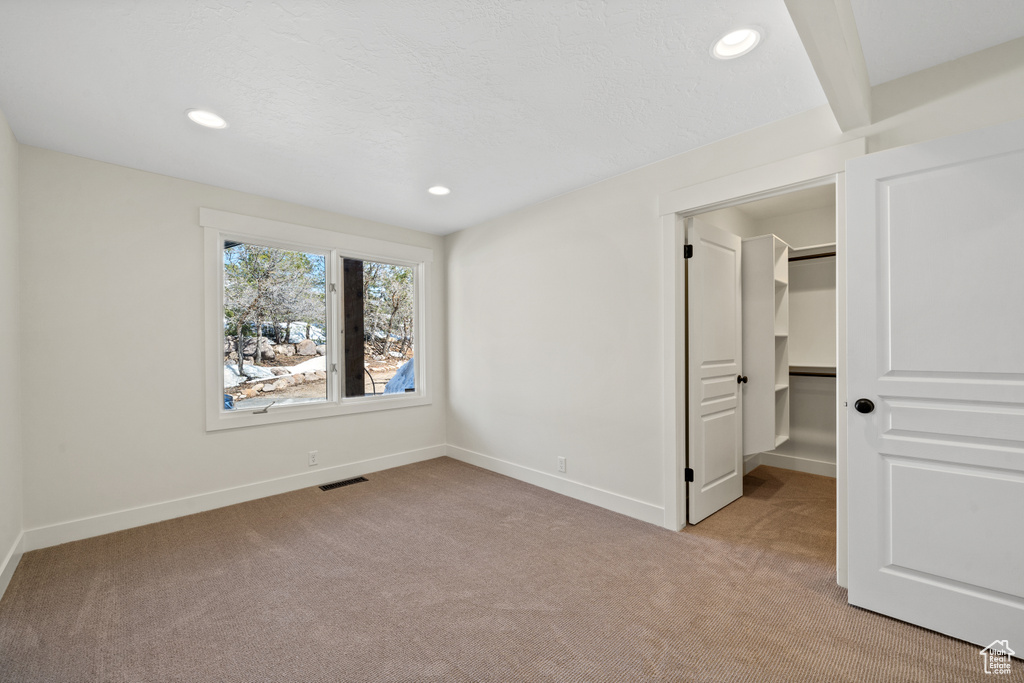 Unfurnished bedroom featuring light colored carpet, a walk in closet, and a closet