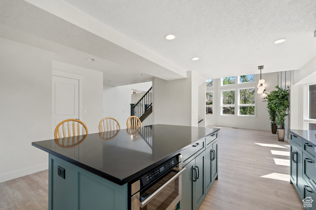 Kitchen featuring decorative light fixtures, a kitchen island, light hardwood / wood-style flooring, a textured ceiling, and oven