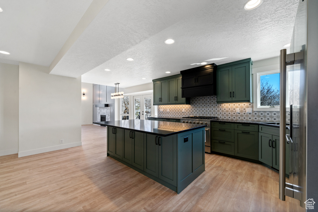 Kitchen featuring stainless steel stove, custom range hood, hanging light fixtures, and light wood-type flooring