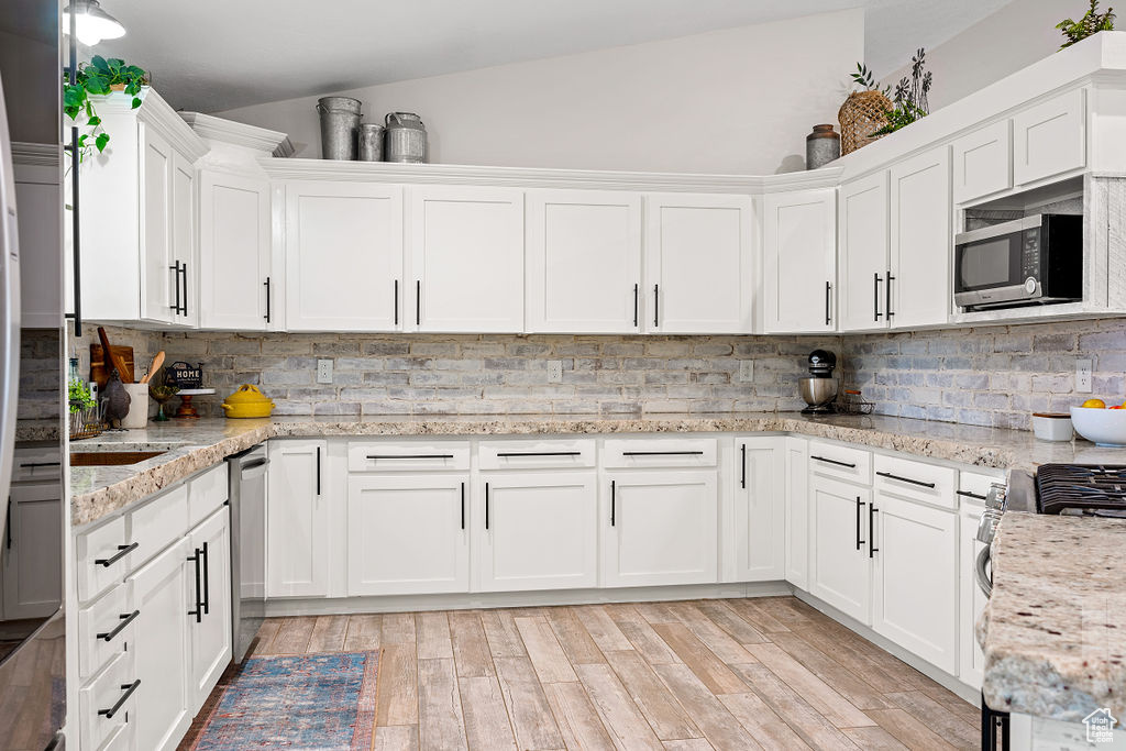 Kitchen with light hardwood / wood-style floors, white cabinets, tasteful backsplash, and vaulted ceiling
