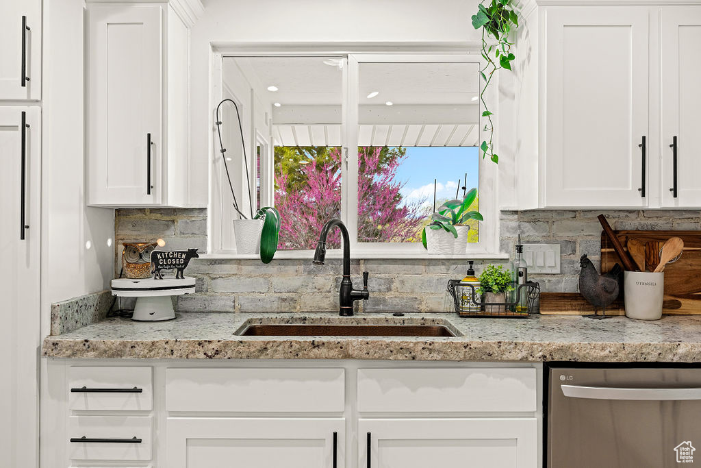 Kitchen featuring stainless steel dishwasher, sink, backsplash, and white cabinets