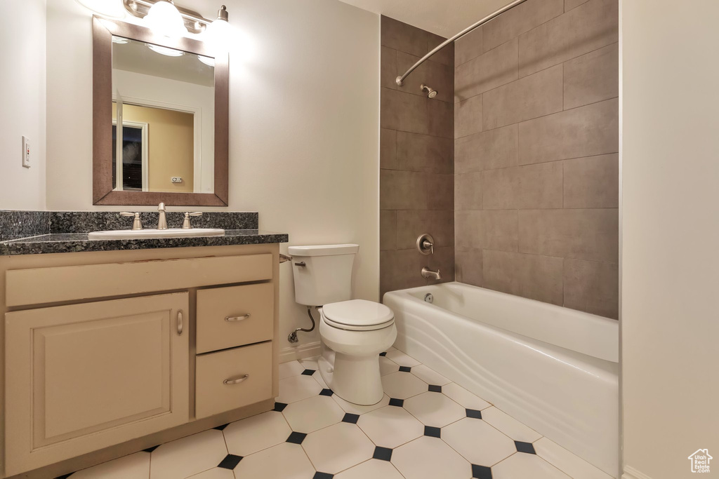 Full bathroom with tile floors, vanity with extensive cabinet space, toilet, and tiled shower / bath