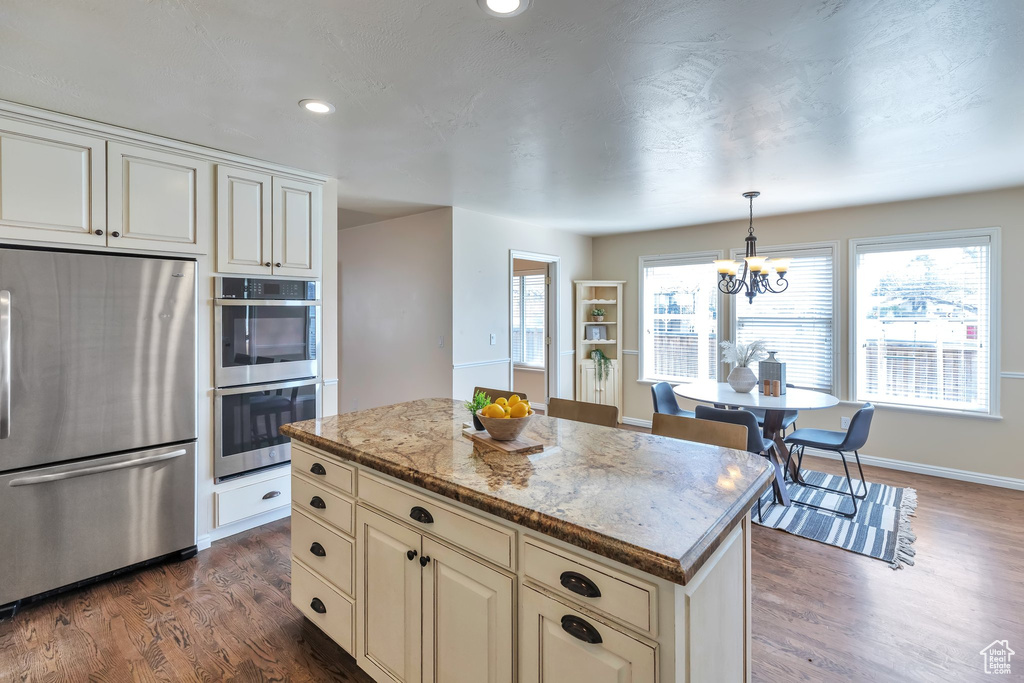 Kitchen featuring a kitchen island, stainless steel appliances, a notable chandelier, light stone countertops, and dark hardwood / wood-style floors