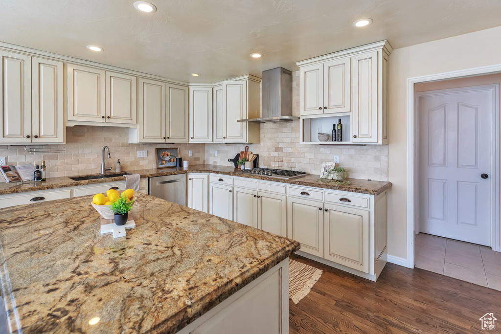 Kitchen with dark hardwood / wood-style flooring, wall chimney range hood, sink, and light stone countertops