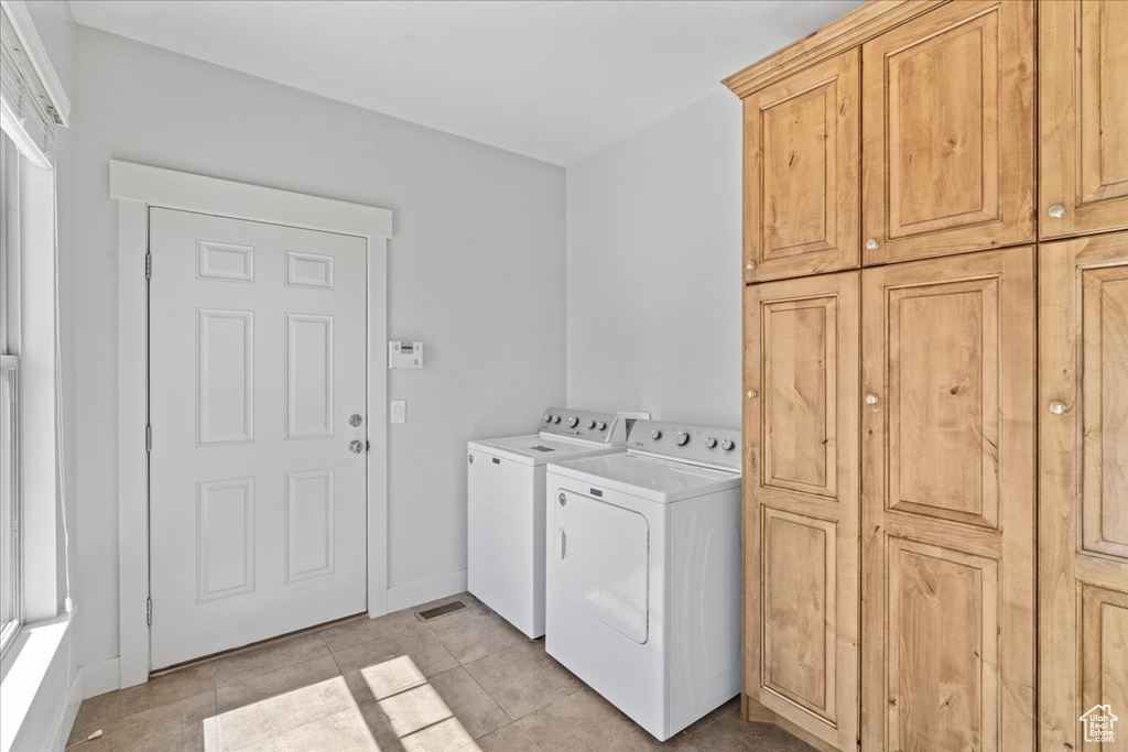 Laundry room featuring separate washer and dryer, cabinets, and light tile floors