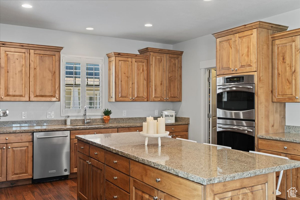 Kitchen featuring a kitchen island, dark hardwood / wood-style flooring, sink, appliances with stainless steel finishes, and light stone counters