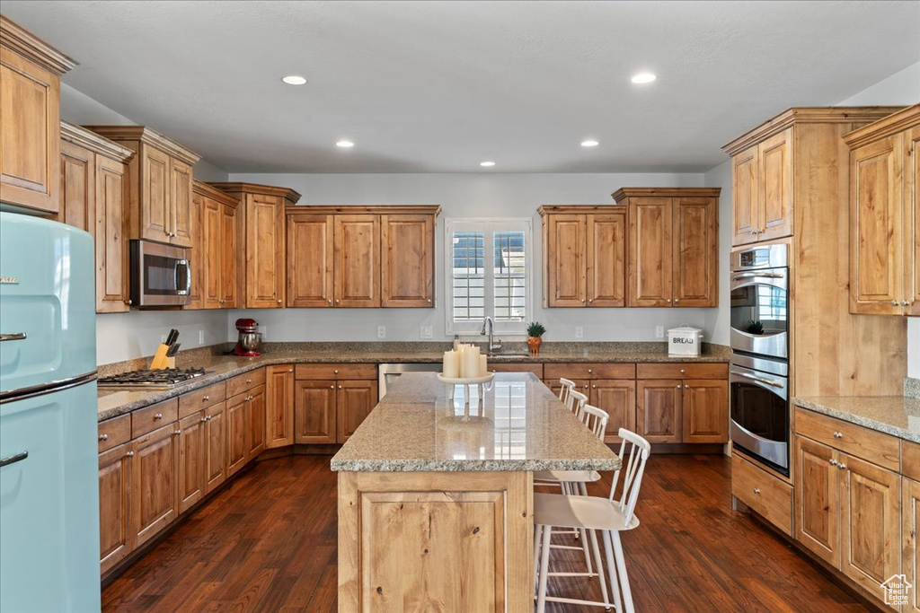 Kitchen featuring light stone countertops, stainless steel appliances, dark hardwood / wood-style flooring, and a center island