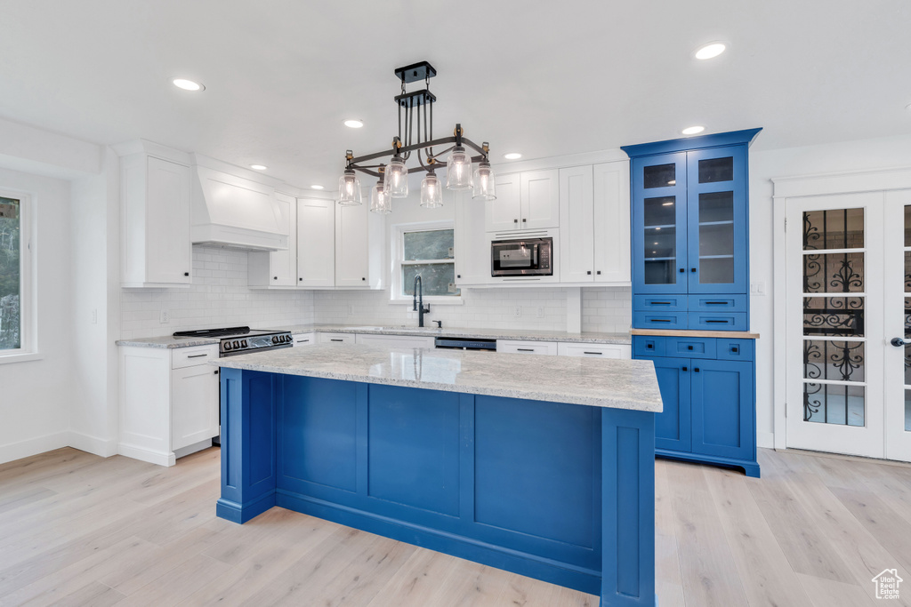 Kitchen featuring decorative light fixtures, stainless steel microwave, light wood-type flooring, and custom range hood