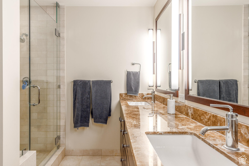 Bathroom featuring a shower with door, dual sinks, oversized vanity, and tile flooring