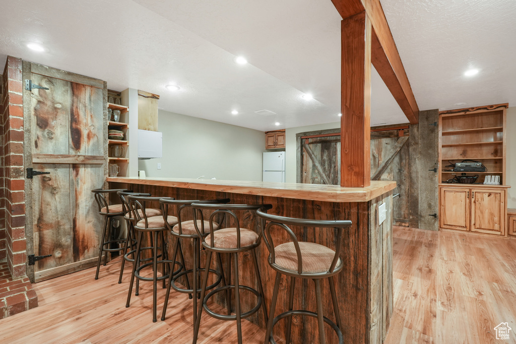 Bar with white fridge and light wood-type flooring